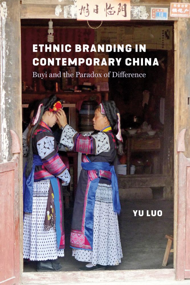 Cover of Ethnic Branding in Contemporary China: Buyi and the Paradox of Difference by Yu Luo. The image shows two Buyi women in traditional dress standing in a wooden doorway. One woman is adjusting the headwear of the other. The title is placed in white text over the upper part of the image, with the author’s name in bold at the bottom right.