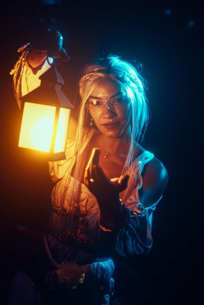 A femme presenting person in white medieval outfit holding a yellow glowing lantern