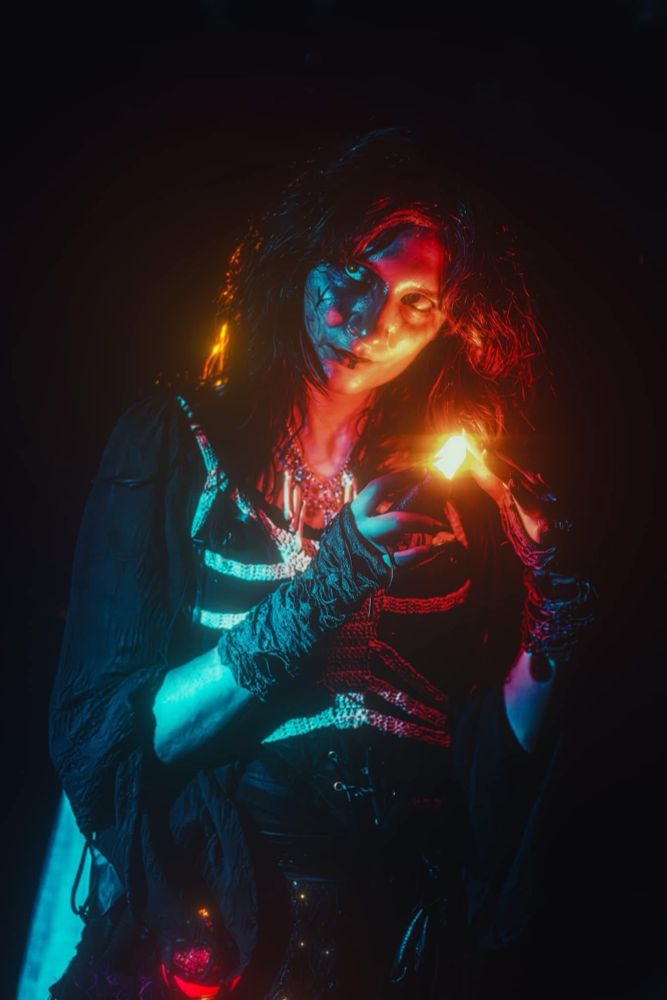 A witchy femme presenting person in black outfit holding a red glowing crystal