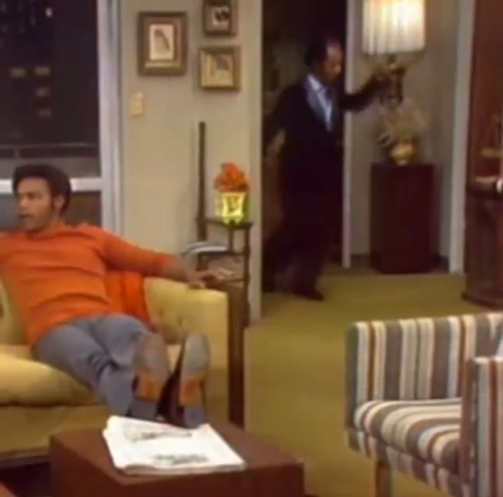 a man in an orange shirt sits on a couch in a living room