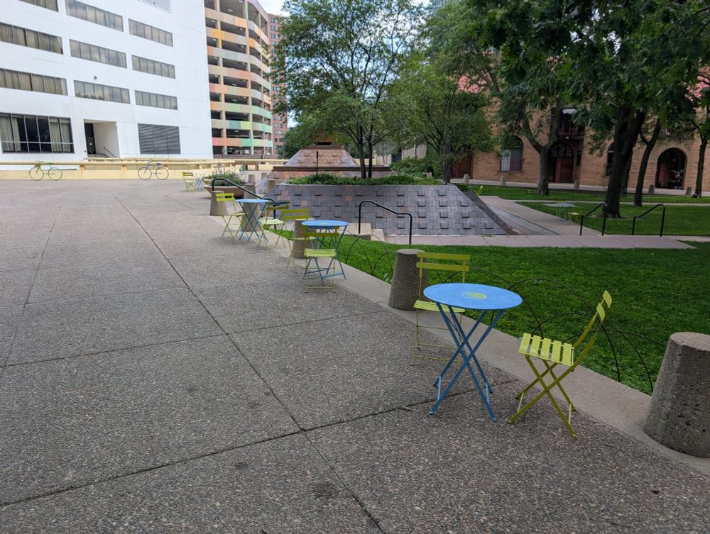 Small table with two small metal chairs next to it, in front of a line of other similar tables and chairs.