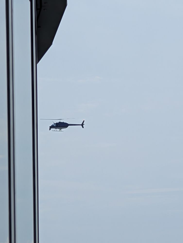 Helicopter in sky with equipment mounted to front. 