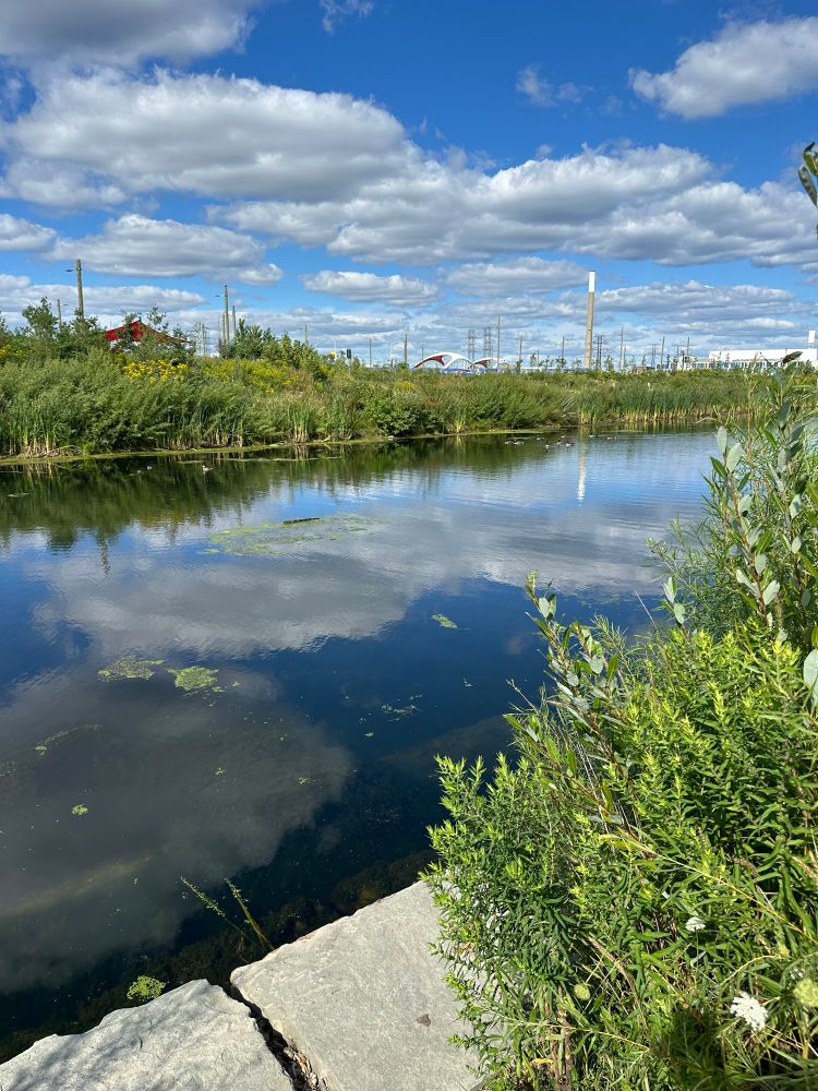 Waterway, green both sides, blue sky with clouds, cherry beach smokestack in background. 