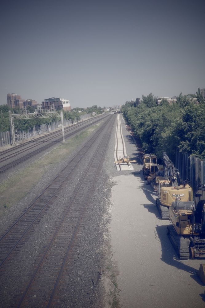 Several large construction machines. No workers or work progress is happening in image. Large site including adjacent park/bicycle infrastructure closed for multiple years. Purpose appears to be a similar track installation. 