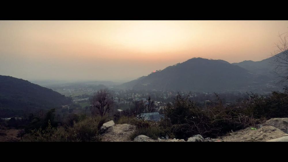An old picture I took shows a peaceful mountain view at sunset. The soft orange glow is visible in the sky somewhere in the lower Himalayan mountains of India. 
