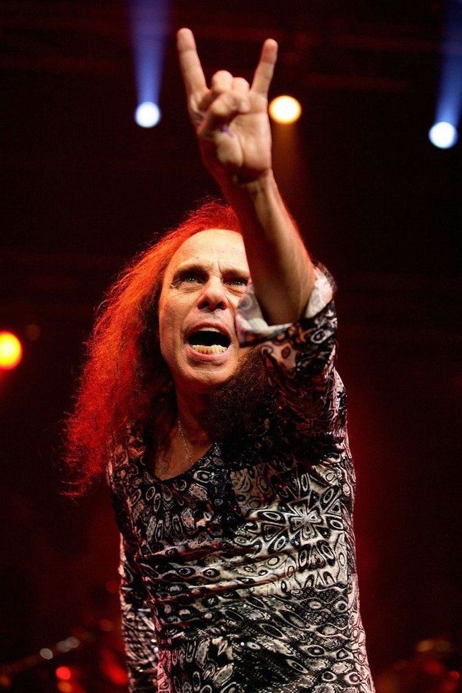 Ronnie James Dio on stage with his left arm outstretched his hand in the form of devil horns which he invented 