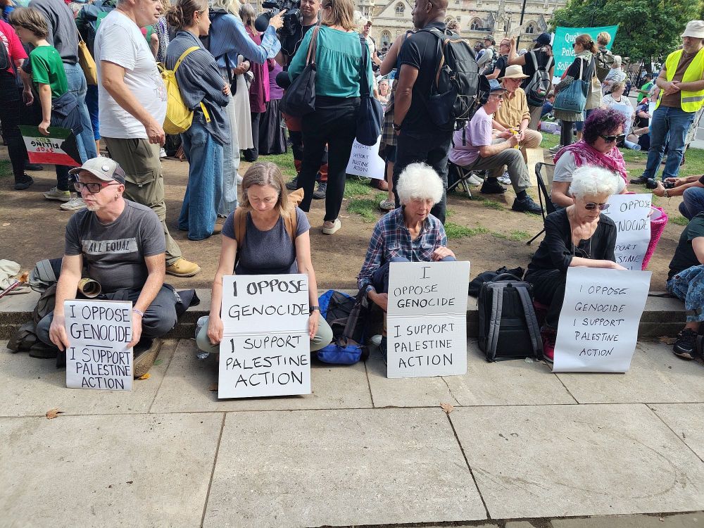 Four people sat in Parliament Square with placards opposing the ban on Palestine Action 