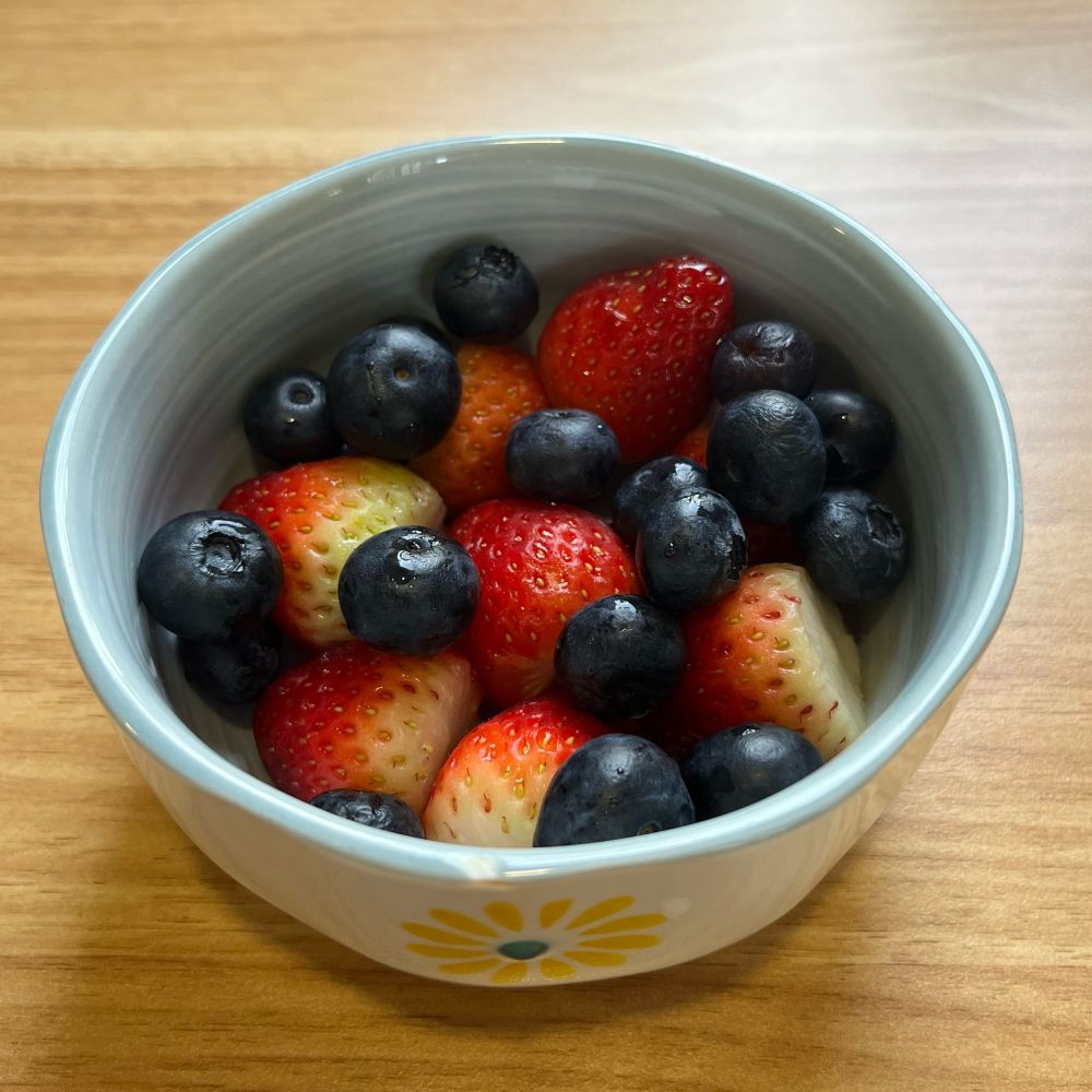 a white and blue bowl full of strawberries and blueberries