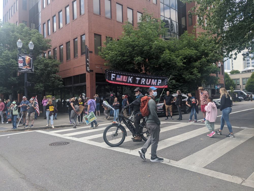 Protester in Portland on bicycle with a large banner over his head that says "F**K TRUMP".