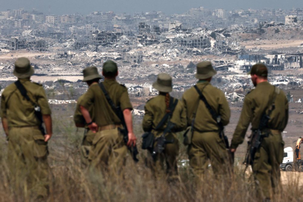 Six soldats de l'armée israélienne regardent des bâtiments détruits dans la bande de Gaza alors qu'ils se tiennent à la frontière avec le territoire palestinien, le 13 août 2025, tandis que la guerre entre Israël et le groupe militant palestinien Hamas se poursuit.

Jack GUEZ / AFP 