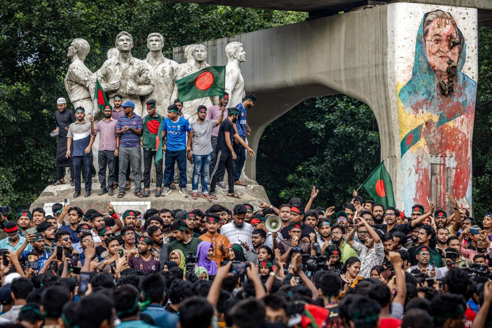 Des étudiants scandent des slogans lors d'une manifestation près de l'université de Dhaka, dans la capitale, le 12 août 2024, pour exiger que la Première ministre destituée du Bangladesh, Sheikh Hasina, soit tenue responsable et jugée. Les manifestants arborent des drapeaux bangladais tandis que la fresque représentant Sheikh Hasina est dégradée avec de la peinture rouge. 

©AFP - Luis TATO