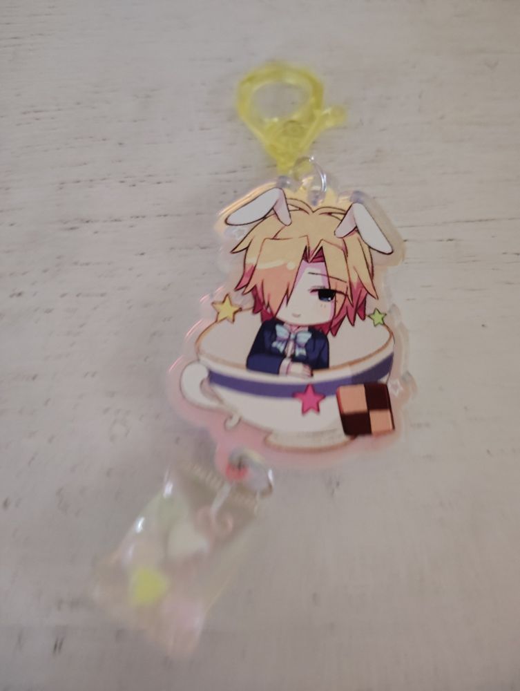  witch's heart alice in wonderland noel levine acrylic keychain. art by the creator is IZ [you can find her on twitter at @/bluestar_iz & @/blueiziz]

noel in his blue suit in a tea cup surrounded by stars [white, pink, yellow, and green]

he has little bunny ears & little sweets are attached to the keychain.