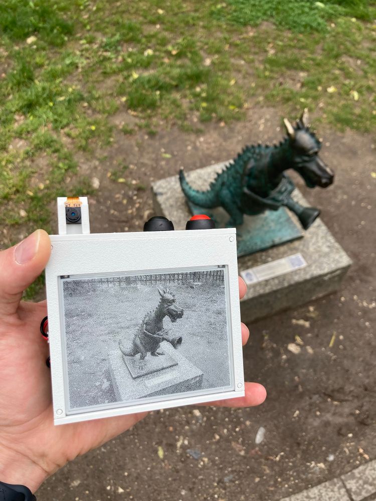 A picture of the eink showing a statue of a dragon holding a camera. Found in a park in Kraków