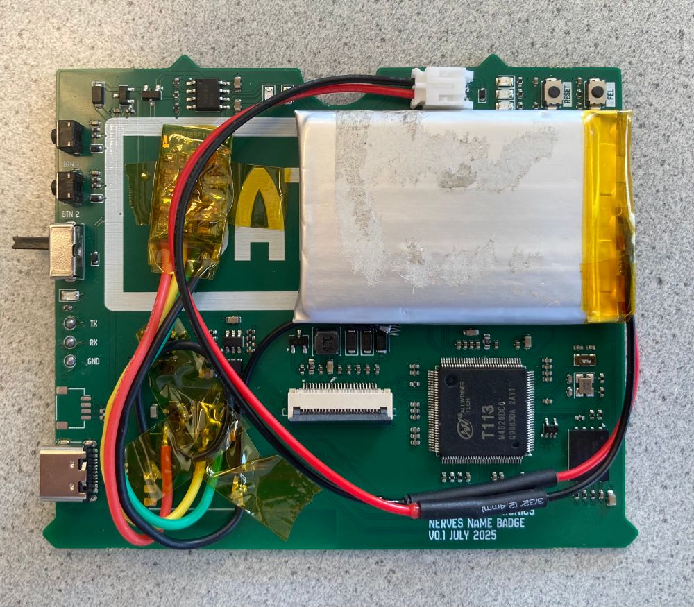 A green circuit board with some colorful wires soldered to a breakout module, and a battery taped to the empty area of the board. The board has a processor in the bottom right corner, a flex cable connector (not plugged in) in the middle, and USB + some switches on the left