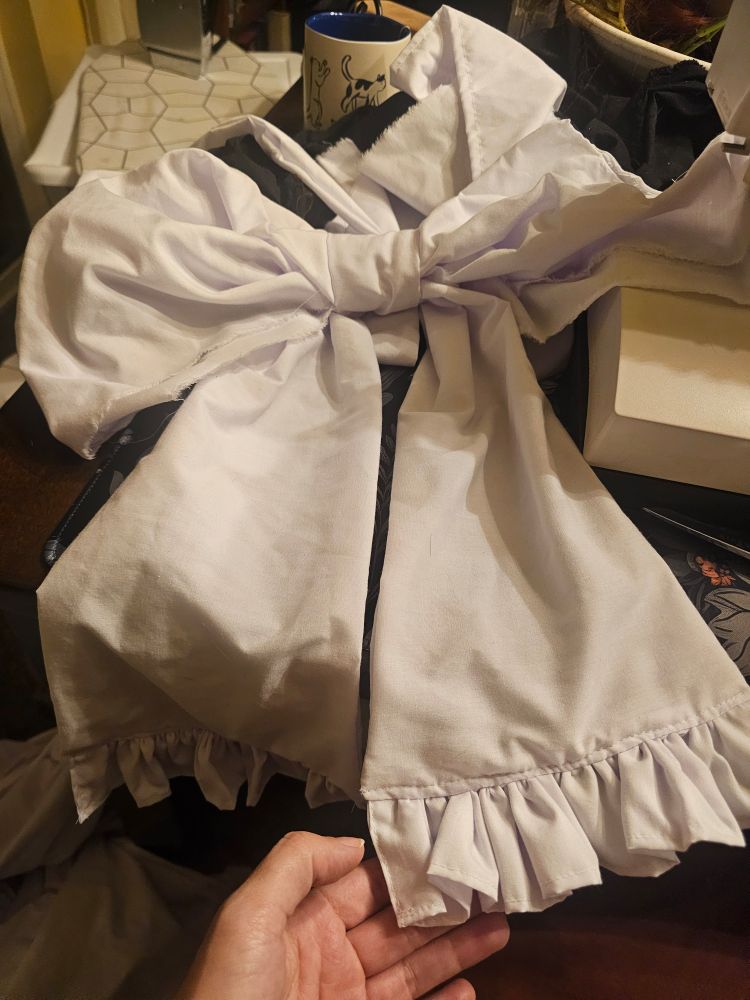 A large white bow. The loop part of the bow has raw fabric edges, but the tails are neatly finished with ruffles at the ends