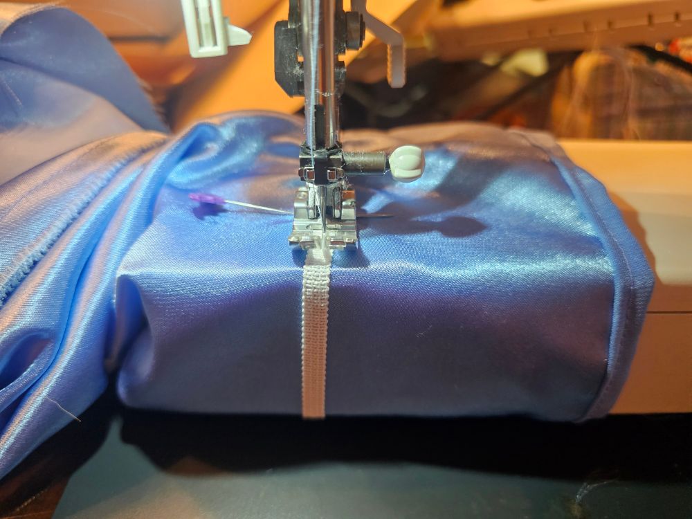 A blue sleeve around the free arm of a sewing machine, with elastic stretched over it