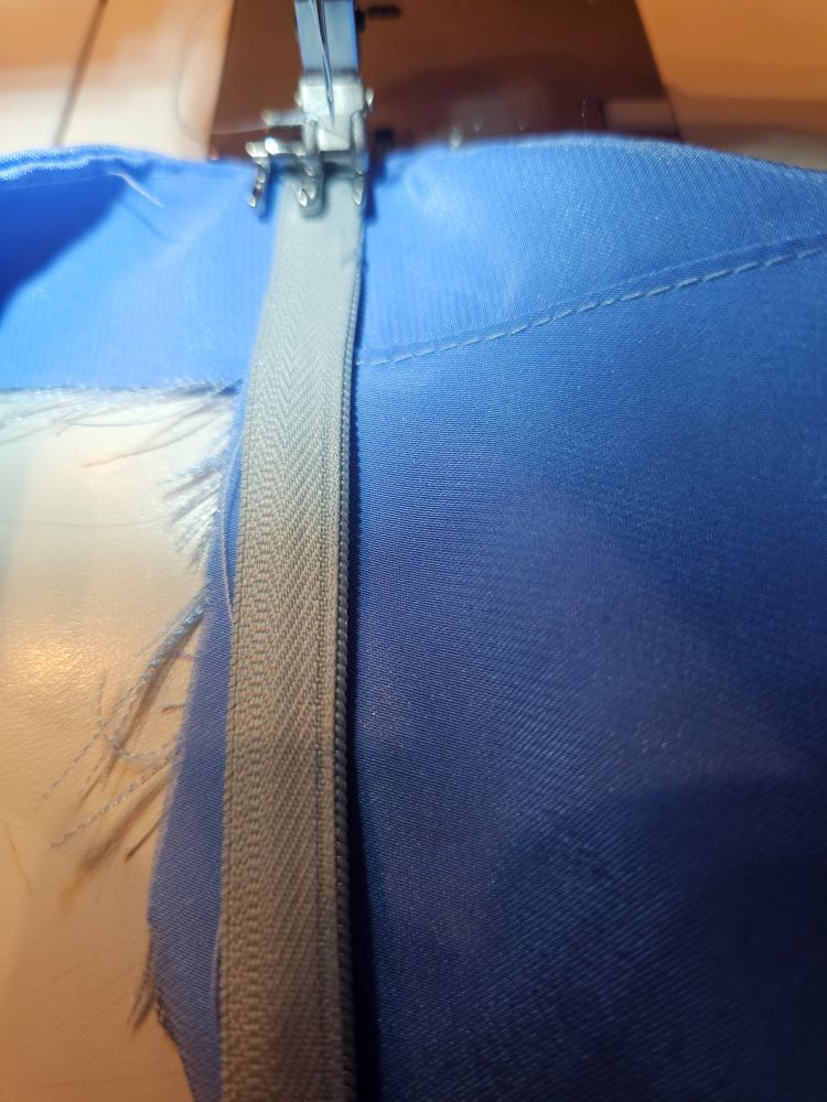 A grey invisible zipper being sewn onto a blue garment