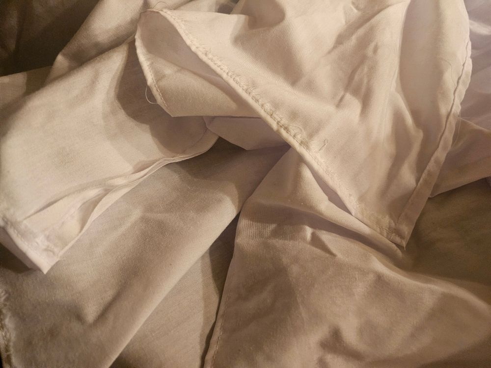 Close up of a single turn hem, a double turn hem, and a selvage left untouched at a seam on white fabric