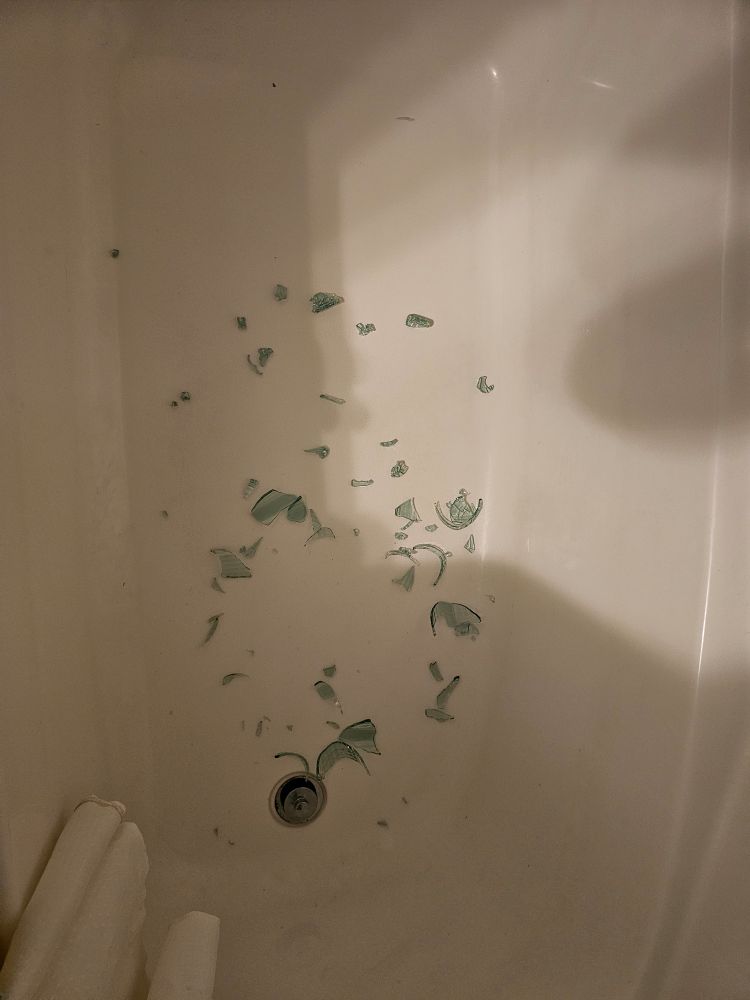 A bathtub with the shattered remains of a green drinking glass in the bottom