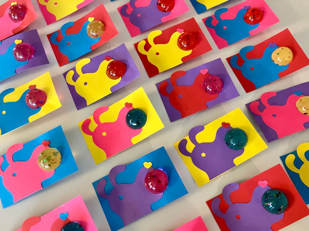 Countertop full of brightly colored cut paper school valentines depicting a floppy eared dog holding a bouncy ball in his mouth. 
