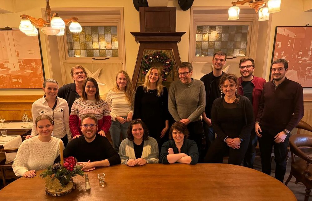 Picture showing 14 people behind a table, in front of a fireplace.
