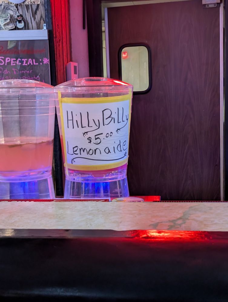 A pitcher of liquid with a sign taped on that says "HillyBilly $5.00 Lemonaide" 