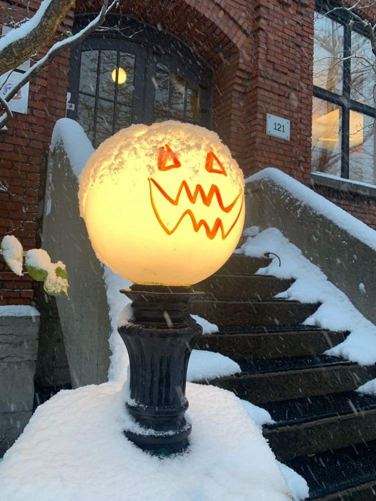 A lit round lamp with a pumpkin face, covered in snow.