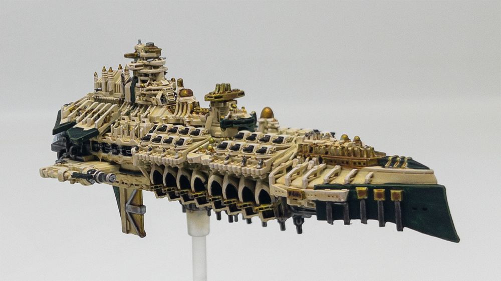 A Warhammer 40,000 Grand Cruiser for the BFG tabletop game. Made by Battlefleet Galaxy and painted by me! She has an ivory hull with a sharp green prow and green playing around her engines. The ship is bedecked with golden domes and detailing. Scores of raked gun turrets sit atop large open plan hangar bays for attack craft. As with all 40K BFG Imperial ships, the Divine Providence looks like a Cathedral had a baby with a Dreadnought era battleship and launched it into space. 

This photo is taken from the front right quadrant of the ship and gives a good view of her bow and starboard gun decks and hangar bays. 