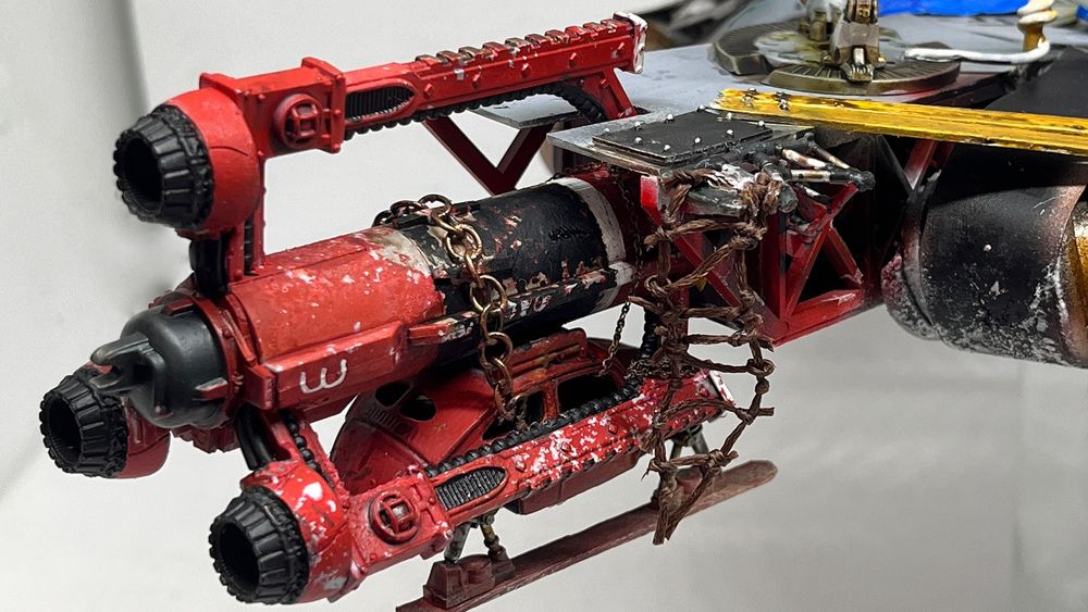 A photograph of the International Wreck Crew Gaslands vehicle Terrorbird Three. The vehicle is a heavily converted Beetle with an enormous rocket chained to the roof, and skids instead of wheels. The rocket is painted bright red, with black accents and a white no.3 on the hull. It is very clearly a post-apocalyptic version of Thunderbird 3. 

In this photo, the car is docked with a large but indistinct black and grey shape.
