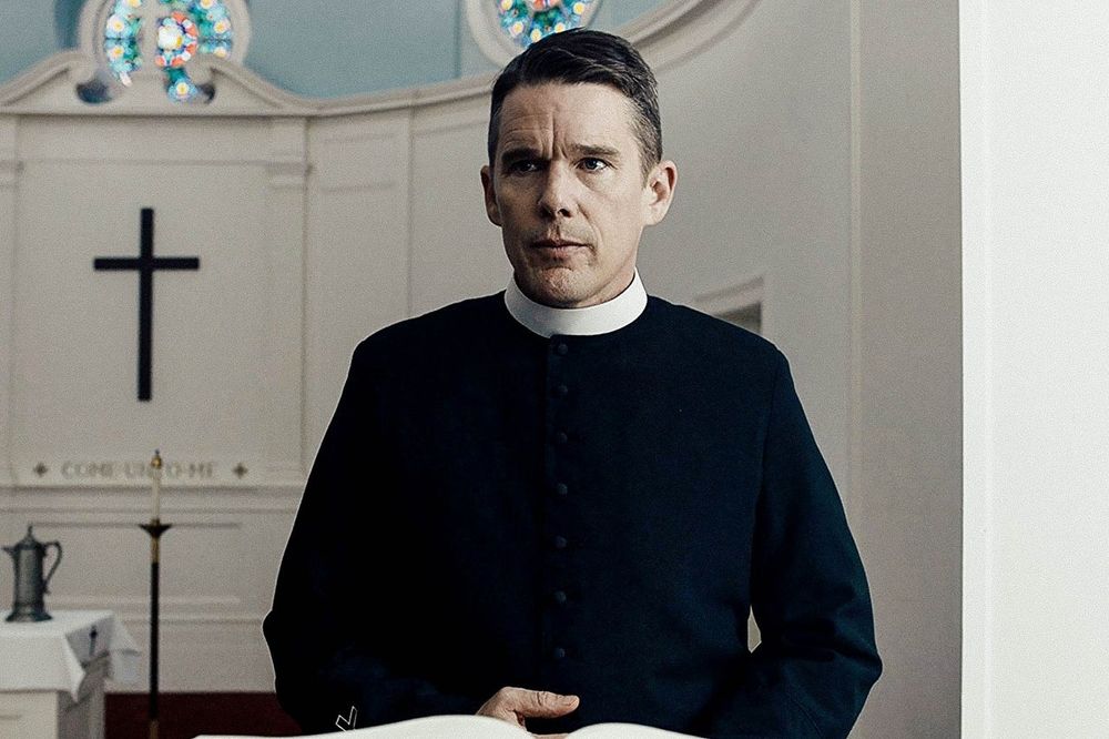 A still from the film FIRST REFORMED: Ethan Hawke, wearing black priest's garments, standing in a church