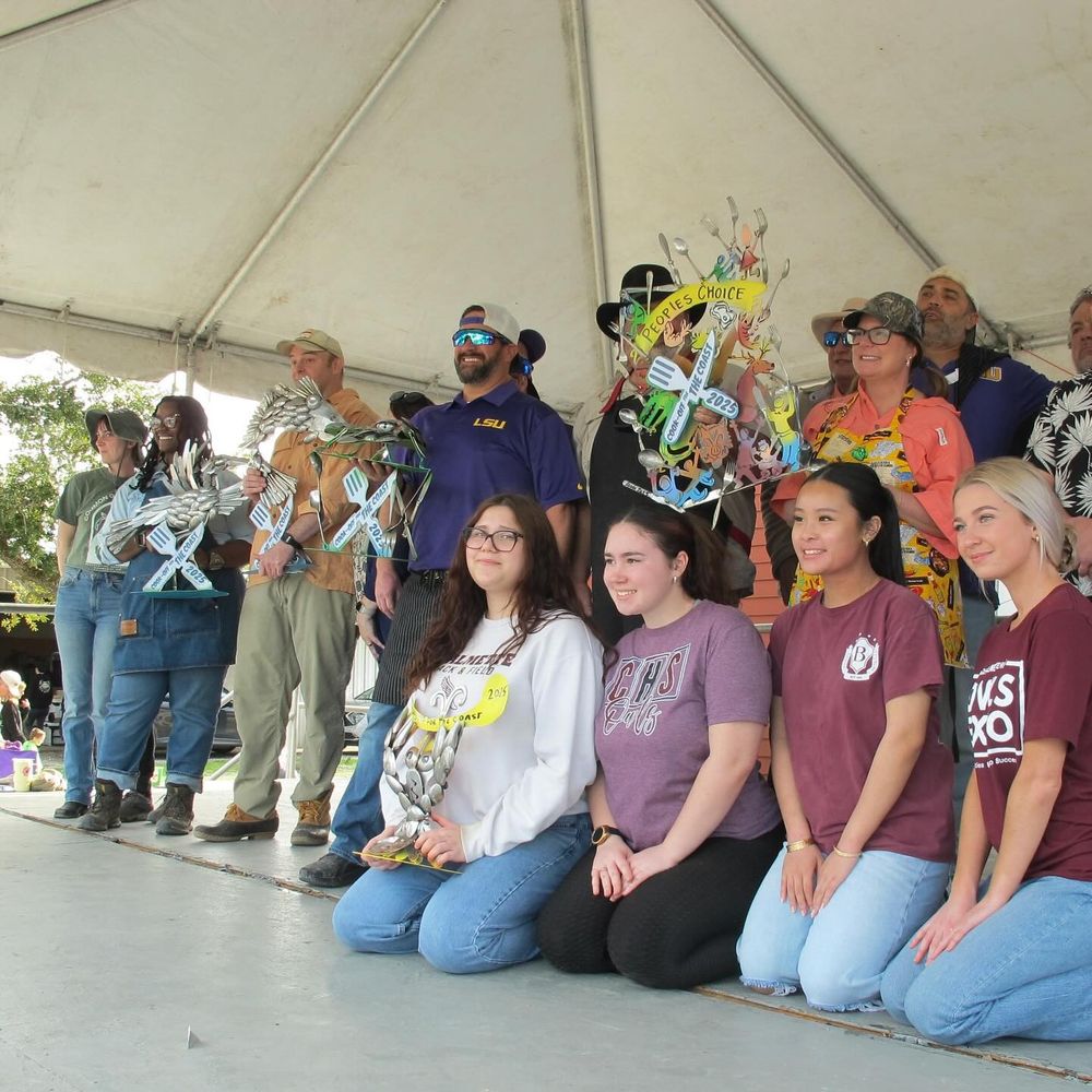 Winning cook teams are standing together to display their handcrafted trophies.