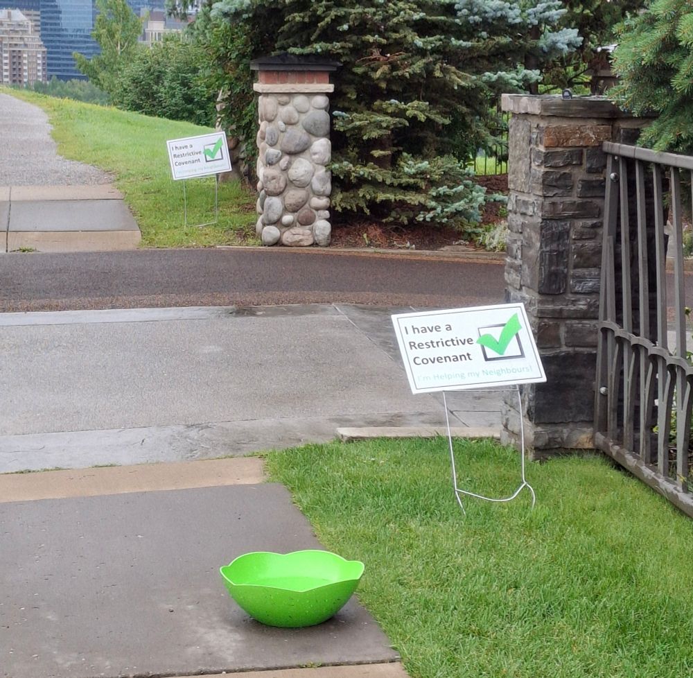 Lawn signs in front of houses that read "I have a Restrictive Covenant. I am helping my neighbours!"