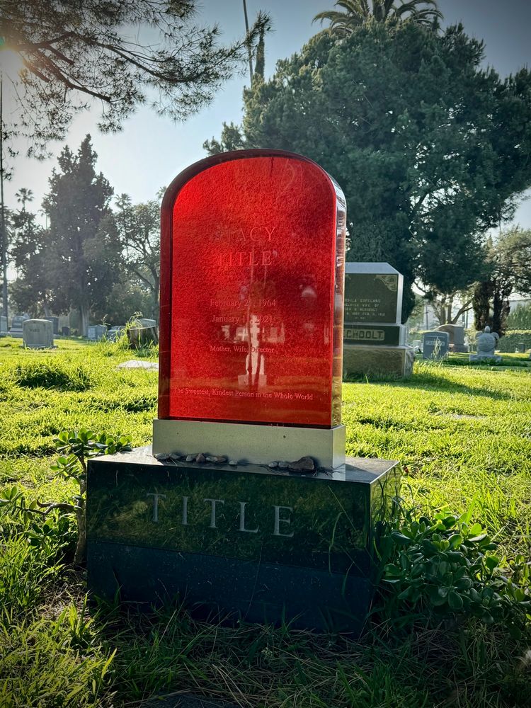 The headstone of Stacy Title made out of thick amber glass with the sun illuminating it