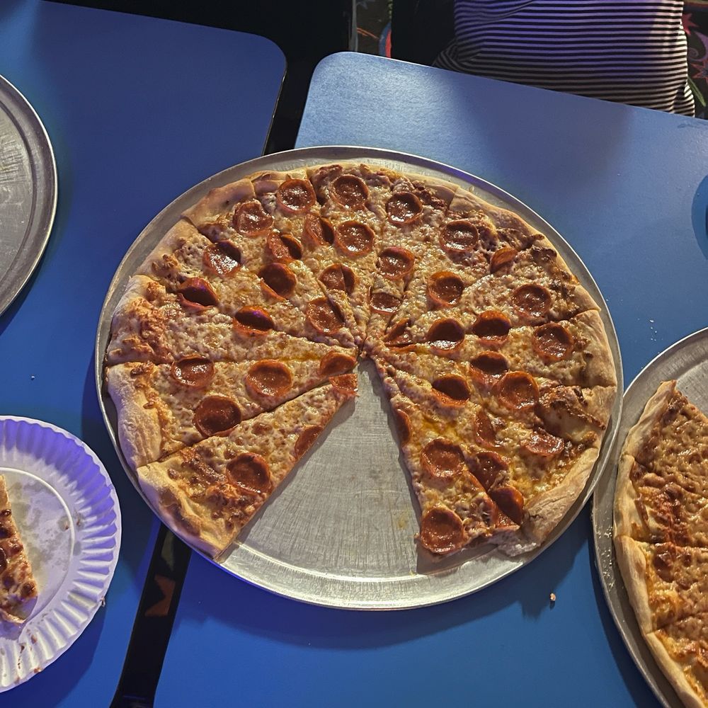 A pepperoni pizza cut into 16 slices on a royal blue cafeteria-style table; a Proustian memory.