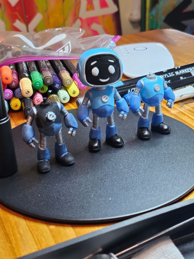 Three in-production images of Robo Kid on a black stand in front of a bag of markers of various colors. Two figures have no head. The middle figure is complete.