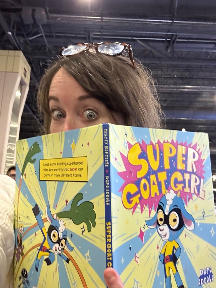 White woman peeking out from behind an opened cot of Super Goat Girl. 