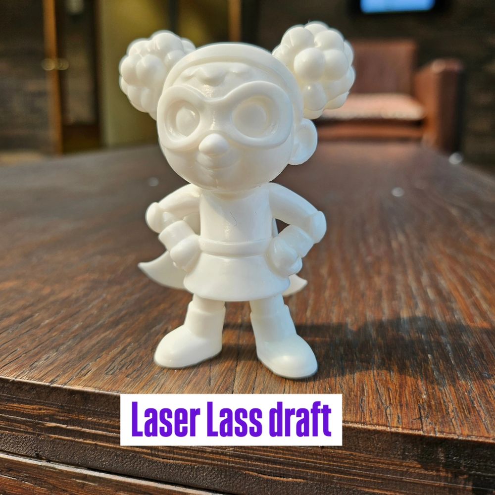 A blank Laser Lass figurines in white resin labeled Laser Lass showing a girl with a cape, boots, skirt, and goggles.