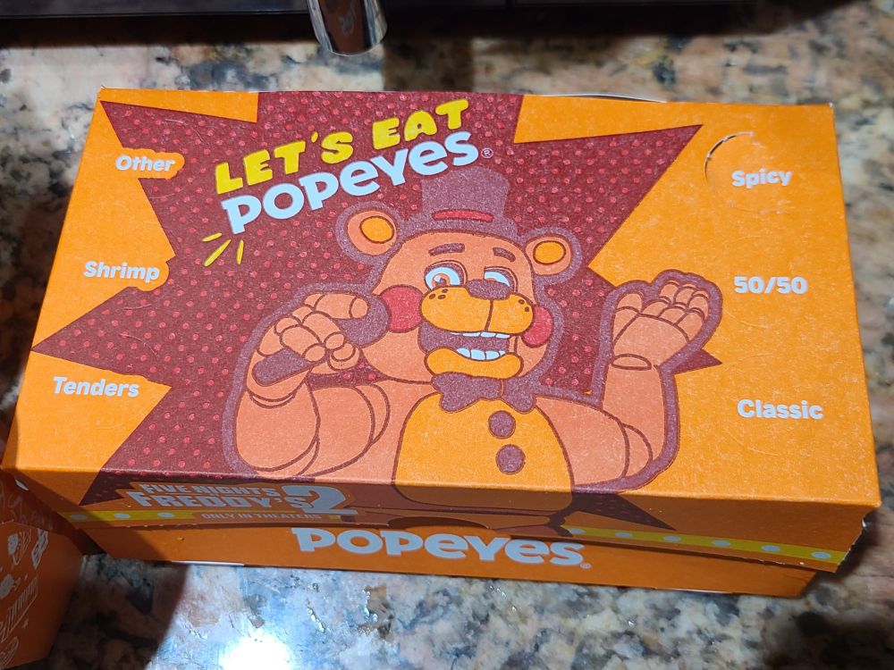 picture of the freddy fazbear box from Popeye's, showing Toy Freddy with the words "Let's Eat Popeyes" above him