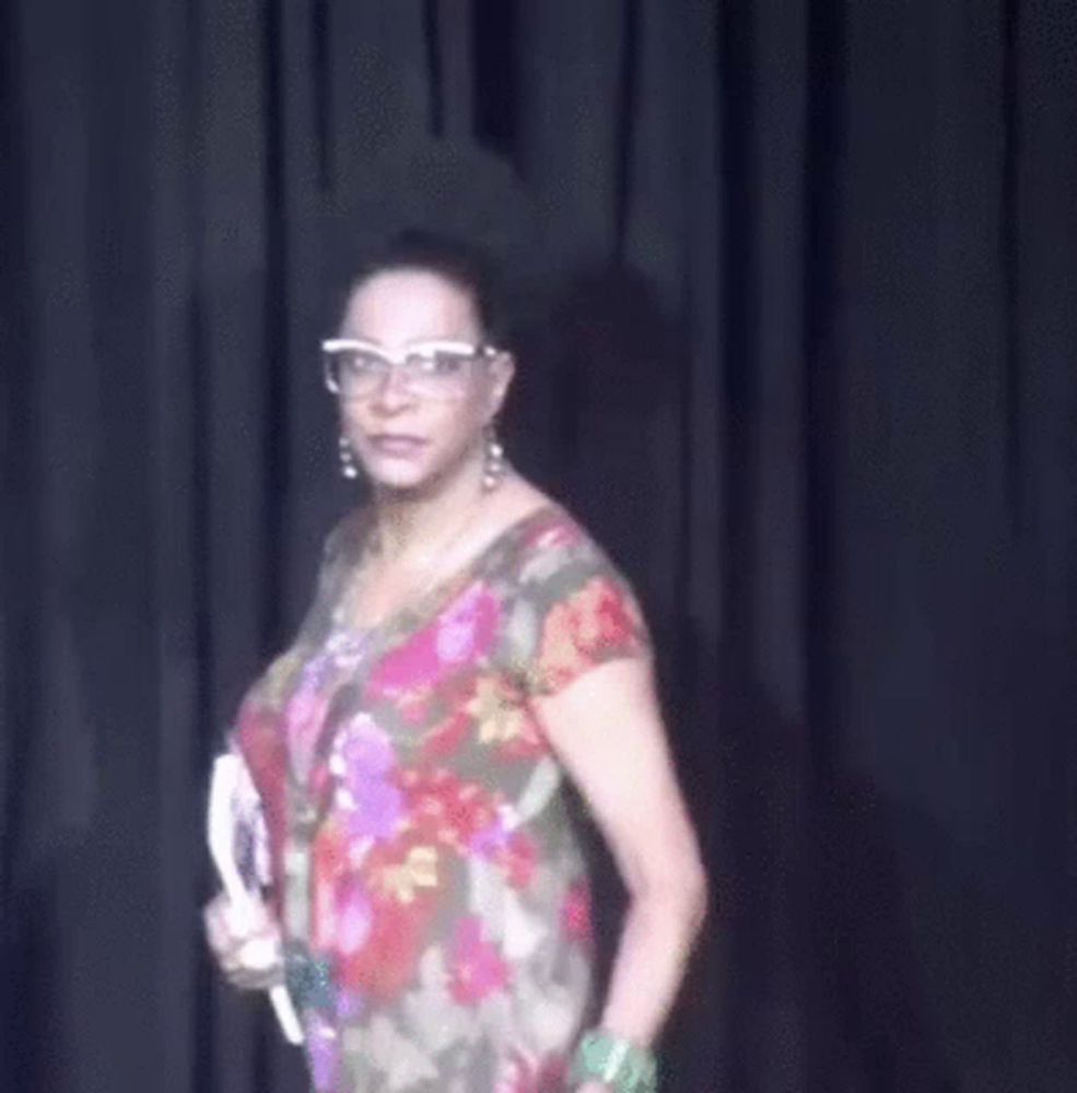 a woman wearing glasses and a floral dress is holding a book