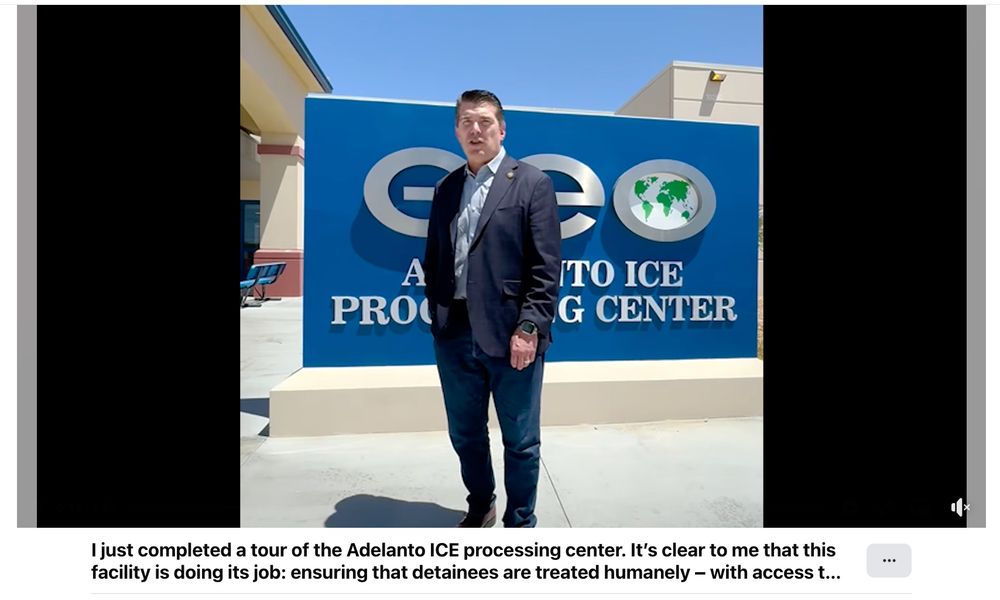 Screenshot of a video: A man in a navy blazer, jeans, and a congressional pin stands in front of a large blue sign that reads “GEO Adelanto ICE Processing Center.” The facility building is visible behind him under a clear blue sky. Caption below the image states: “I just completed a tour of the Adelanto ICE processing center. It’s clear to me that this facility is doing its job: ensuring that detainees are treated humanely — with access t...” (text is cut off). 