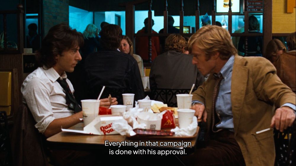 Dustin Hoffman e Robert Redford como Carl Bernstein e Bob Woodward em "Todos os Homens do Presidente", em uma mesa de lanchonete com sanduíche e batatas do Mc Donald's.