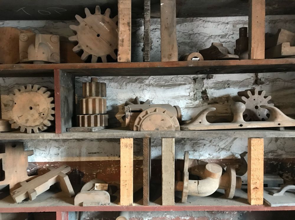 Three shelves against a whitewashed wall, piled with wooden cogs and other wooden shapes 