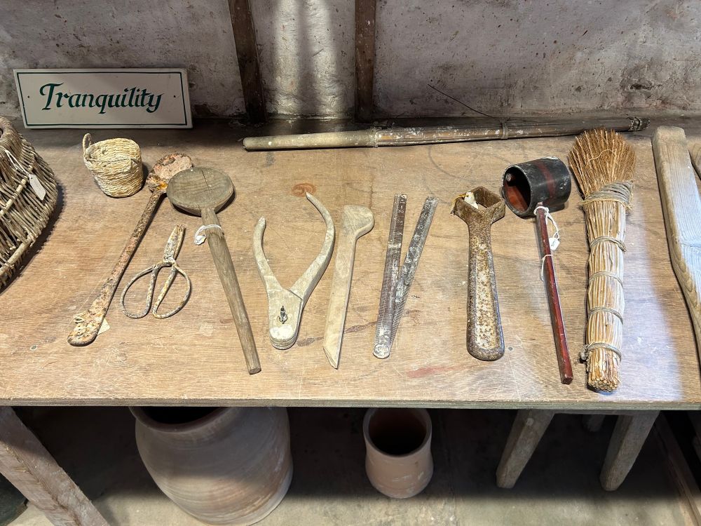 A wooden shelf with various scoops, callipers, brushes, scissors, spoons. A propped up sign reads “Tranquillity”.