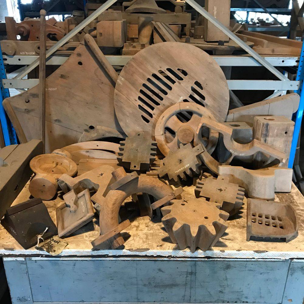 A table and shelves piled with wooden carved cogs and pipes and bits 