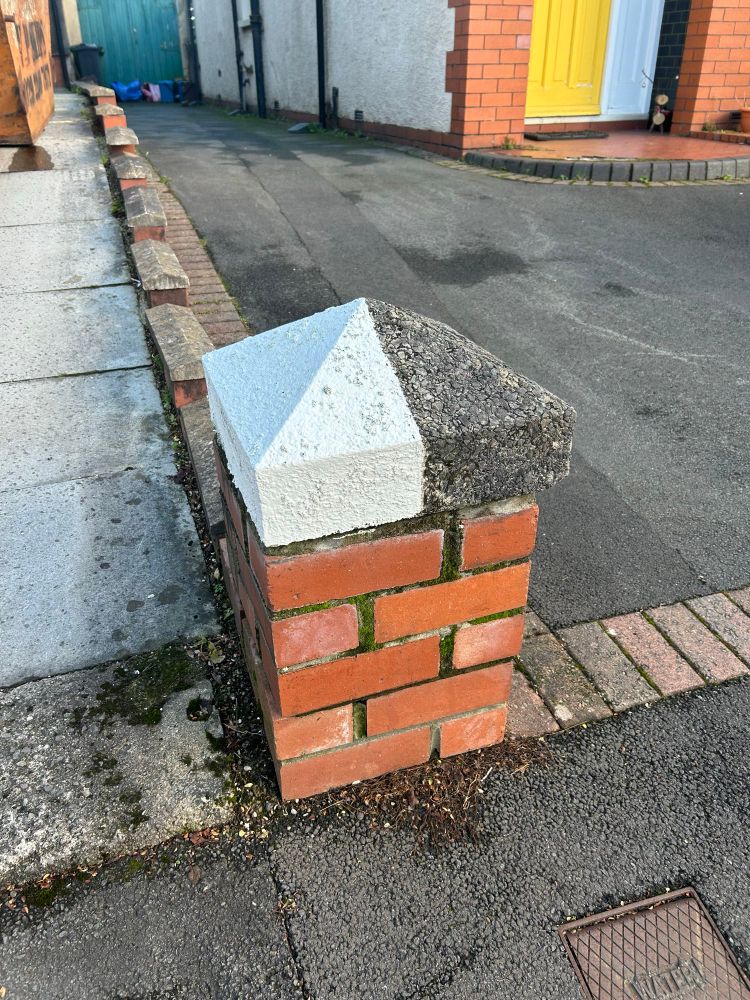 A squat brick pillar topped by an arrowhead cap. Half has been left as raw grey concrete, the other half very carefully painted white