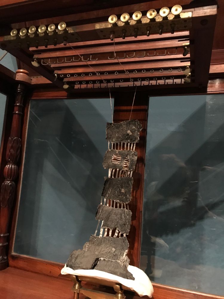 Looks like a piece of papyrus is being tortured? Threads attached to the top of it rise up to wind around brass fixings. To be honest it’s pretty hard to figure out what is going on! 