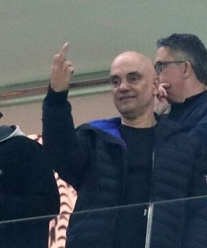 Ministro Alexandre de Moraes no estádio vendo jogo do Corinthians visivelmente despreocupado com as sanções do cheetos de peruca mostrando o dedo do meio em formato de recado como quem diz "vai avisando qualquer coisa" 