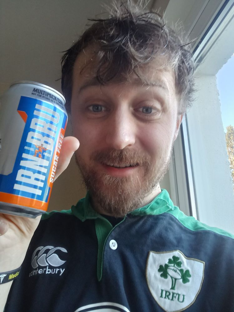 A scruffy man in an Ireland rugby shirt holding a can of sugar-free Irn Bru.