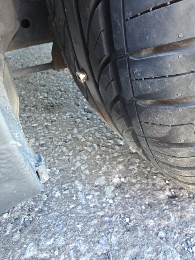 Close up side view picture of one of my car tires. It has a huge screw sticking out of it.