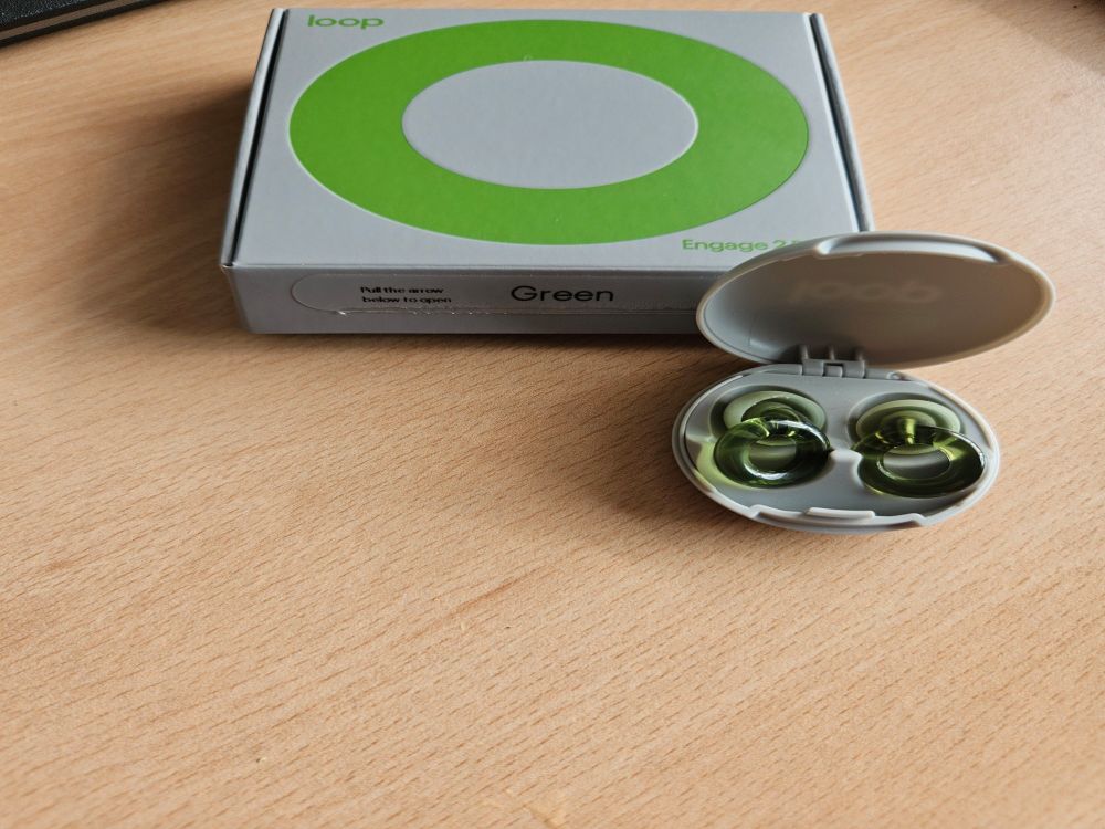 Cardboard box with green circle on it beside a small circular plastic case with green earplugs in it